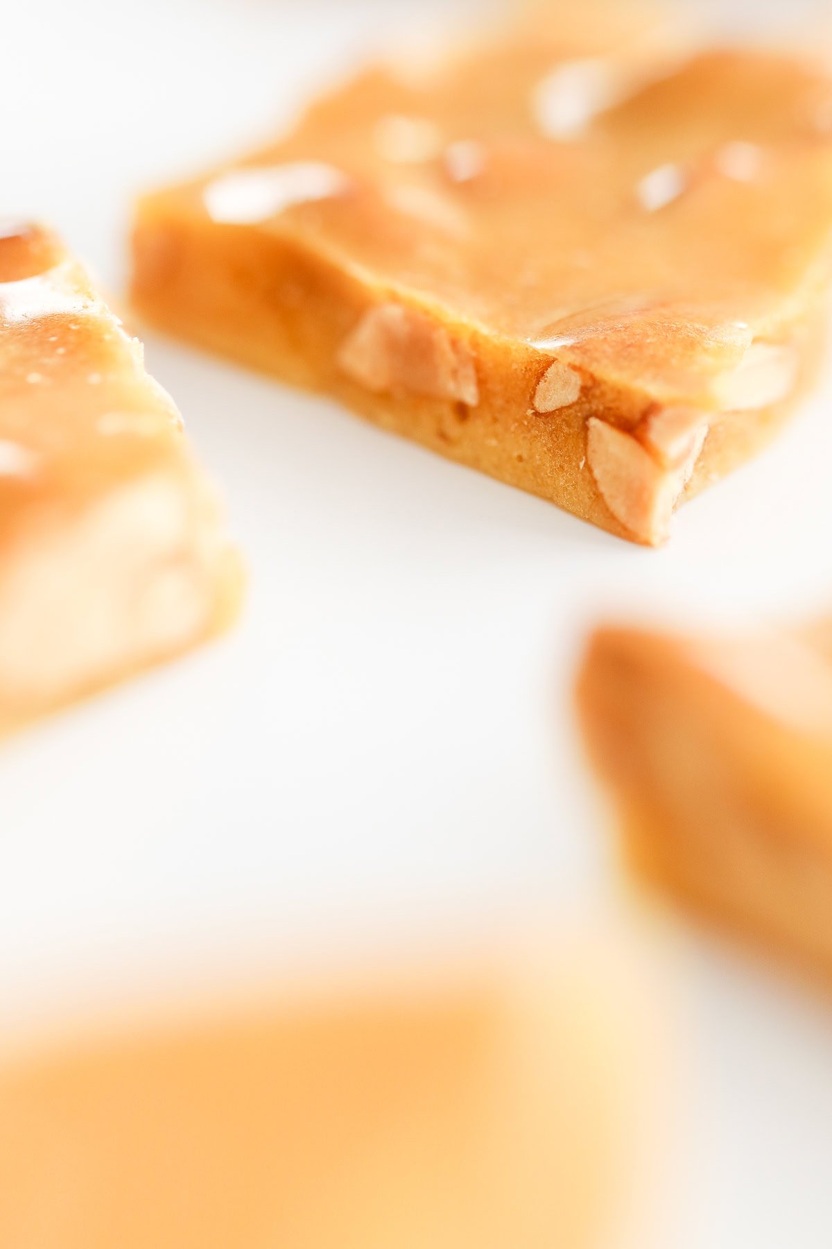 A close-up of a peanut brittle showcases the crunchy delight, with visible nuts embedded within and blurred pieces scattered gracefully in the background.