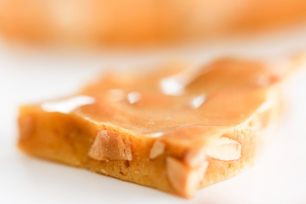 Close-up of a glossy peanut brittle piece with visible peanuts, exuding rich nutty aroma.