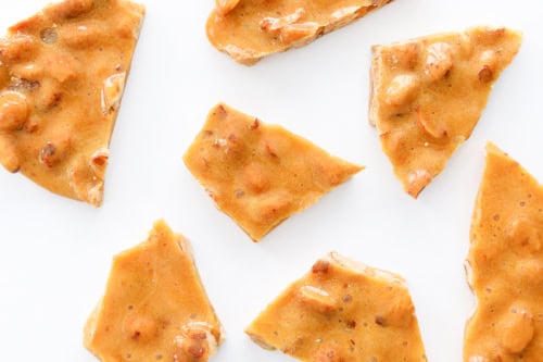 Irresistible shards of classic peanut brittle glisten enticingly on a pristine white background, showcasing the perfect blend of crunchy nuts and sweet caramel.