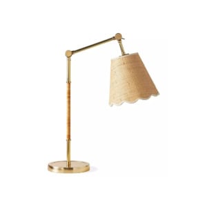 A brass desk lamp with an adjustable arm and a woven rattan lampshade featuring a scalloped edge, offering a chic serena and lily look for less, set against a plain white background.