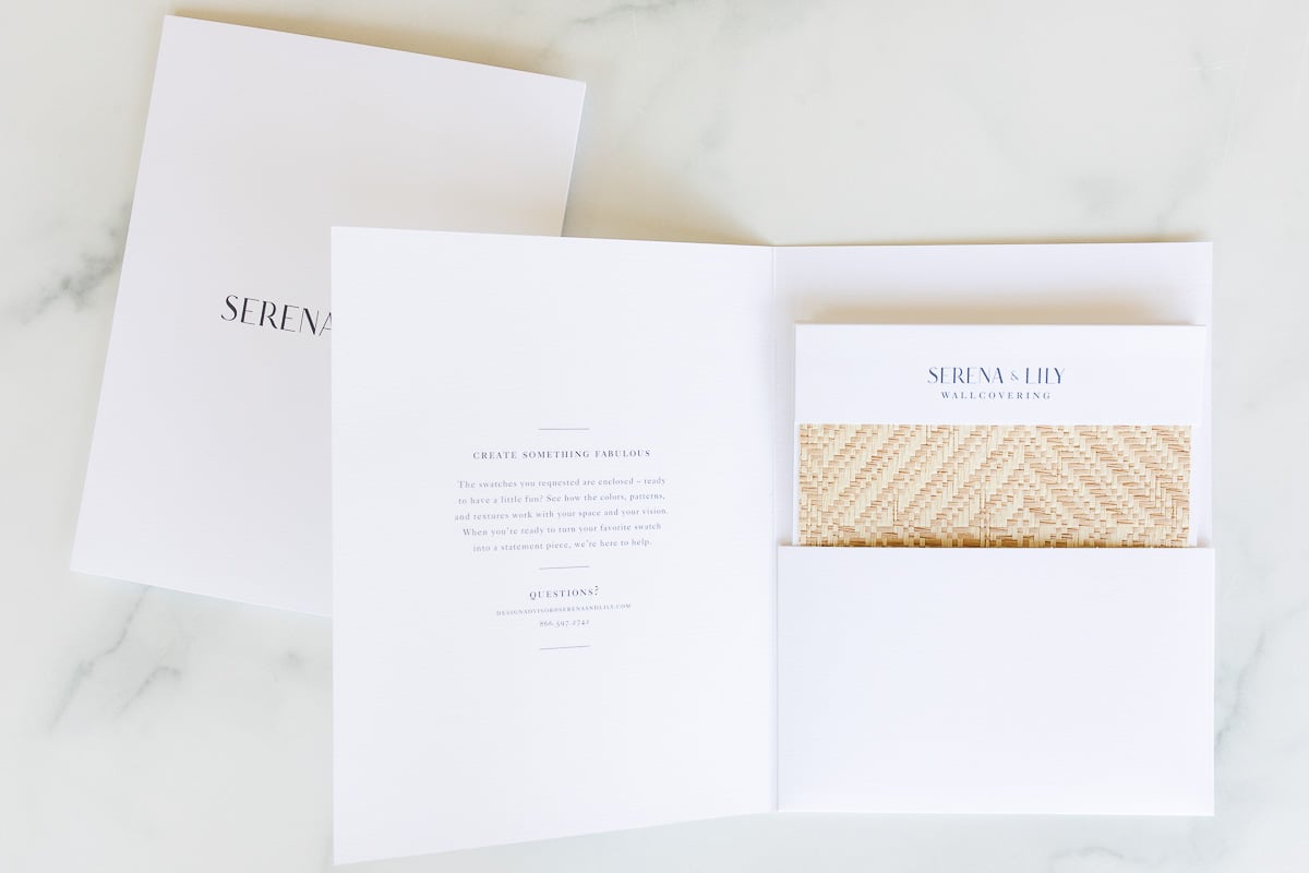 Open folder with a booklet and a patterned sample sheet labeled "Serena & Lily Wallpapering" on a marble surface, showcasing the elegant serena and lily wallpaper collection.