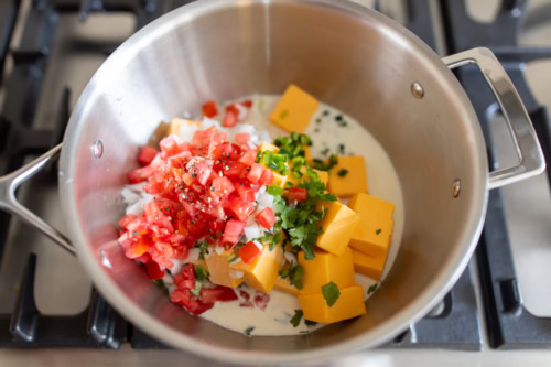 In a pot on the stove, diced tomatoes mingle with creamy Velveeta cheese dip, while cream, chopped onions, green peppers, and cilantro join the mix.