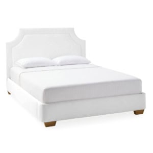 A white upholstered bed with a rectangular headboard, two white pillows, and a white mattress on wooden legs offers a Serena and Lily look for less.