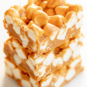 Three stacked squares of butterscotch and peanut butter marshmallow bars on a white background.