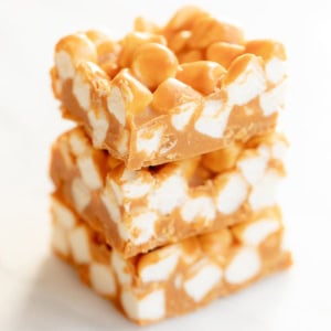 Three stacked squares of Peanut Butter Marshmallow Squares showcase a delightful mix of peanuts and fluffy marshmallows nestled in a butterscotch base, all set against a light background.