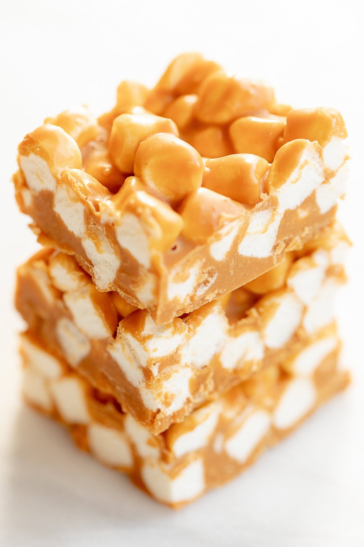 Three stacked squares of butterscotch and peanut butter marshmallow bars on a white background.