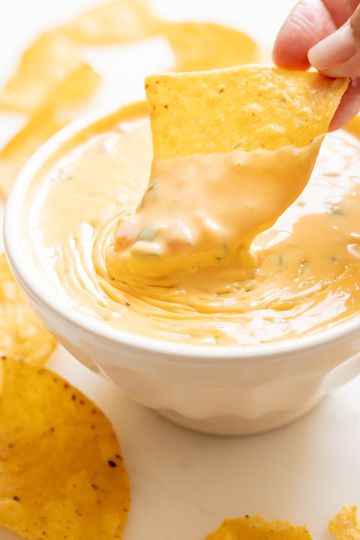 A hand dips a tortilla chip into a bowl of creamy Velveeta cheese dip.