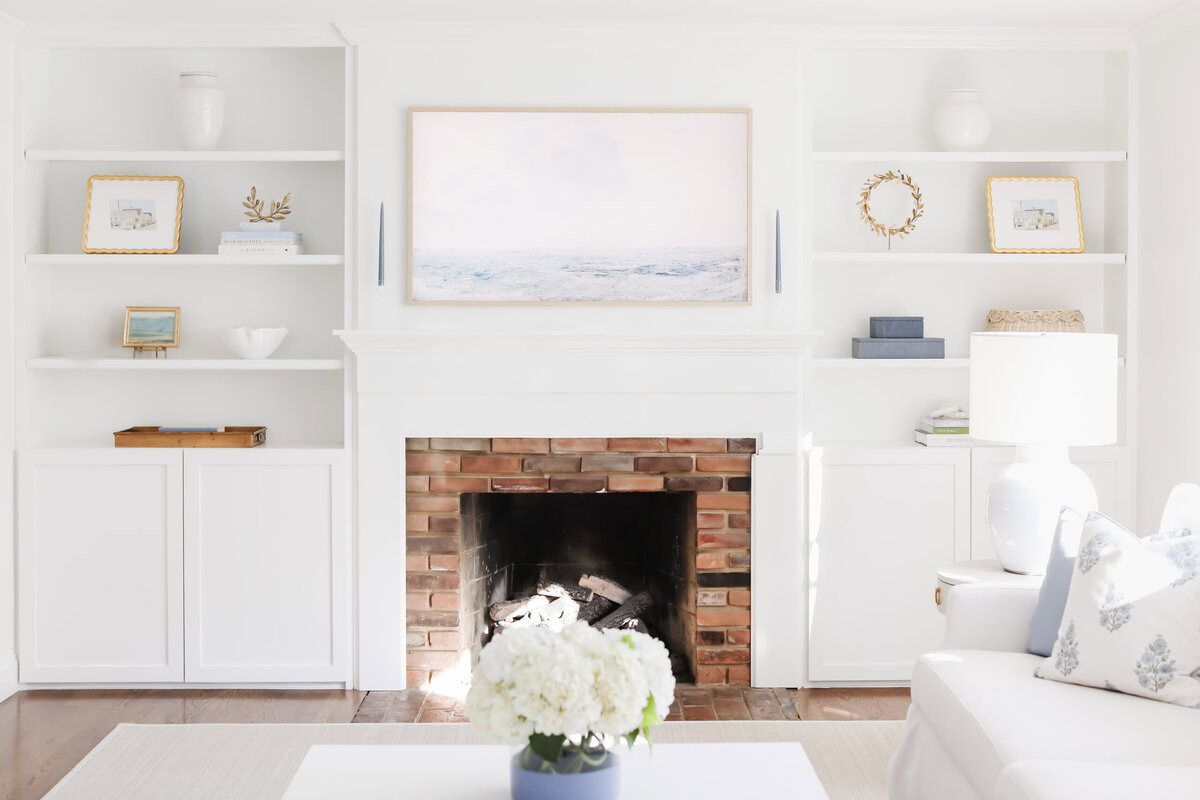 Bright living room with a brick fireplace, white built-in shelves displaying decor, and a framed seascape painting above the mantel—complete the look with the perfect rug size using our handy rug size guide.
