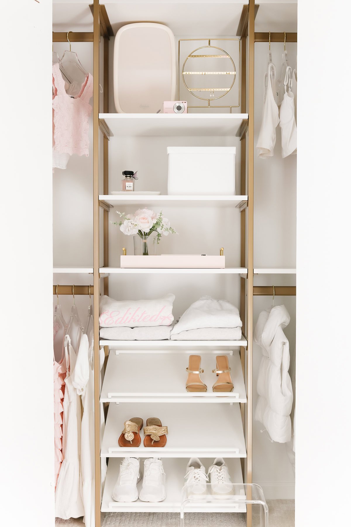 Neatly organized kids closet with shelves displaying pink and white items, folded towels, shoes, and clothes on hangers.