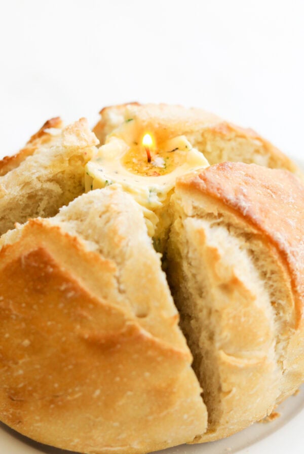 A round loaf of bread with a candle embedded in the center, placed on a white plate.