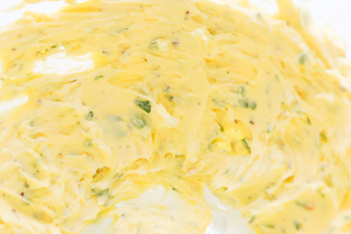 Close-up of creamy butter mixed with green herbs and small flecks of seasoning, spread smoothly over a surface.