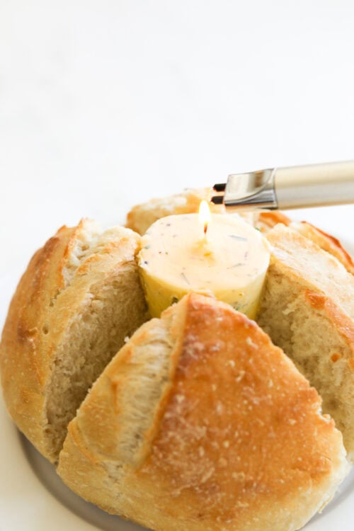 A round loaf of bread with slits, encasing a lit candle in the center, being ignited by a lighter.