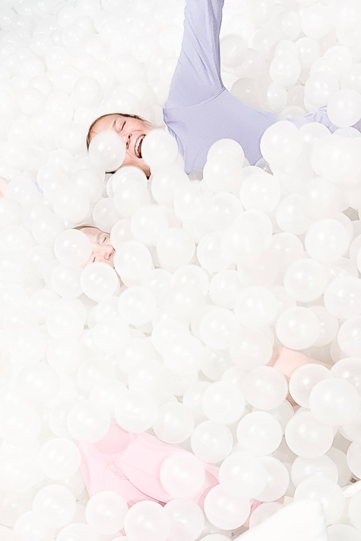 Two people wearing pastel clothing are partially submerged and playing in a large pit filled with white plastic balls, highlighting one of the unique things to do in Branson.