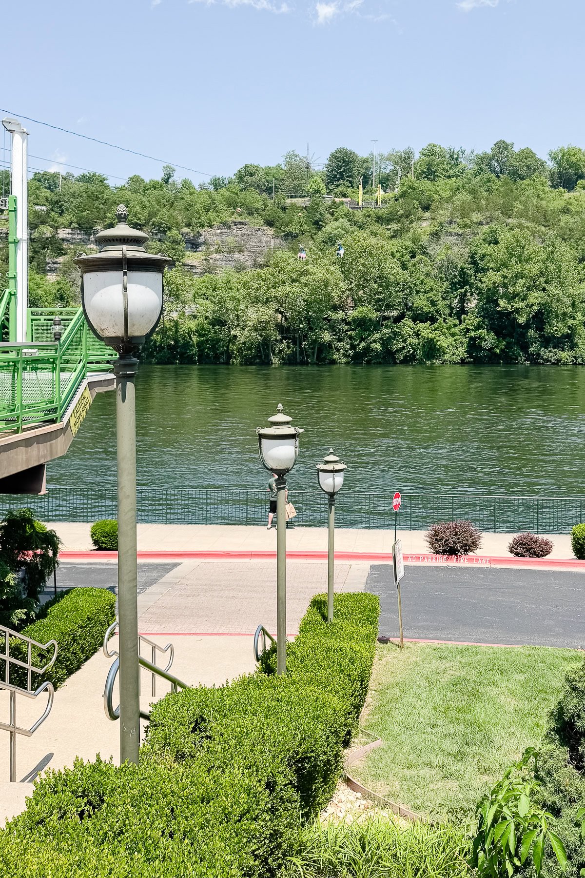 Four street lamps line a walkway overlooking a river, with trees and a hillside in the background under a clear sky—one of the scenic things to do in Branson.