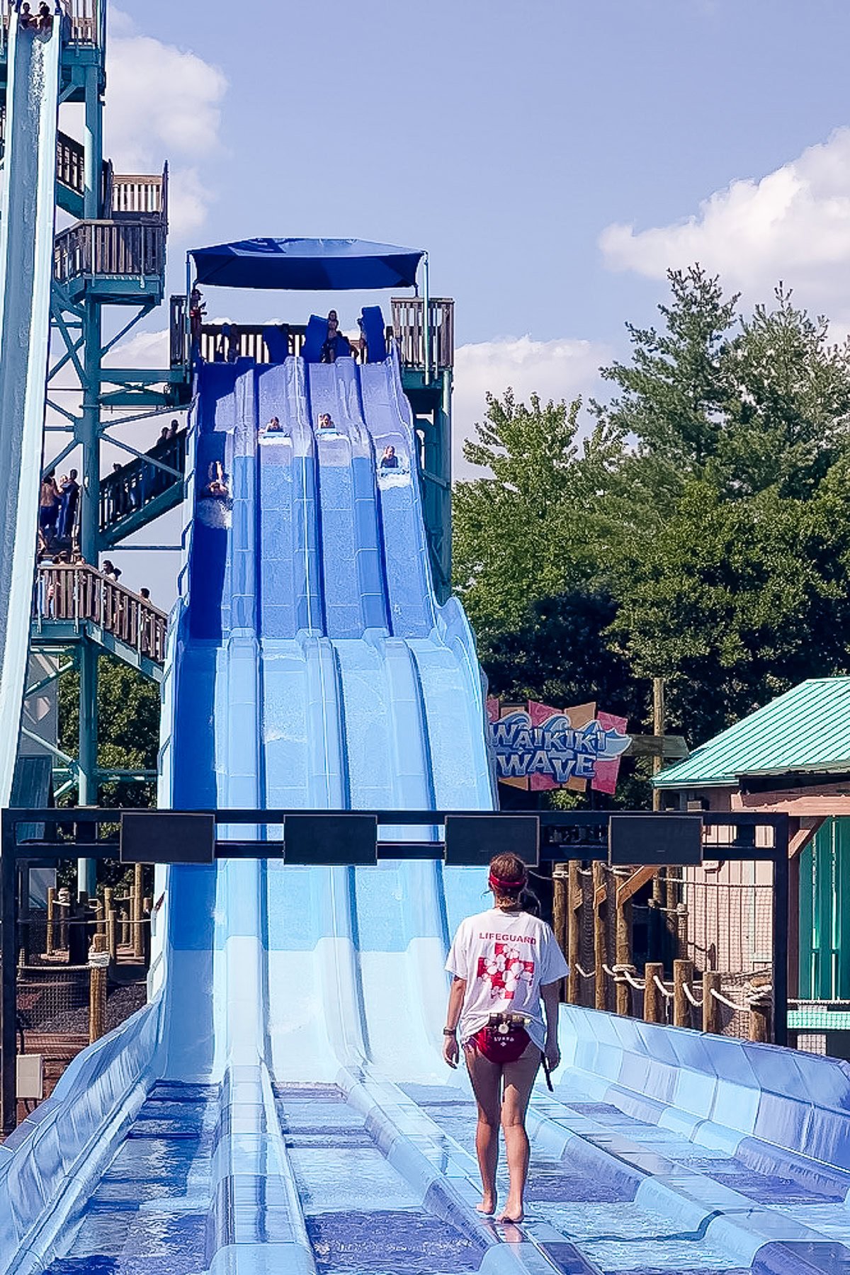 A lifeguard stands at the bottom of a multi-lane blue water slide as several people race toward the finish—one of the exciting things to do in Branson under a sunny sky.