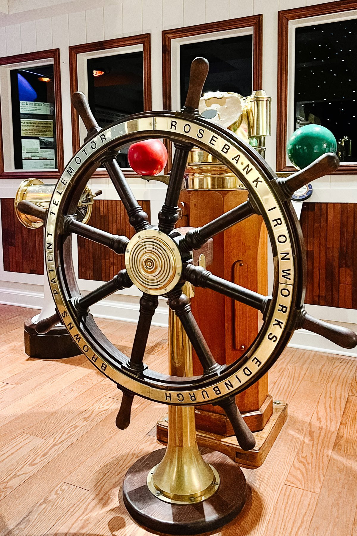 A large brass and wood ship’s wheel labeled