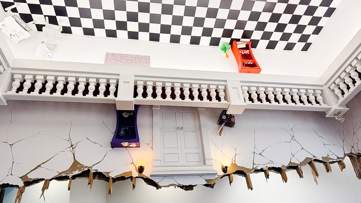 A quirky spot among things to do in Branson—a room with an upside-down design: the ceiling features checkered tiles and suspended furniture, while the floor appears cracked, complete with a vertical door and lamps.