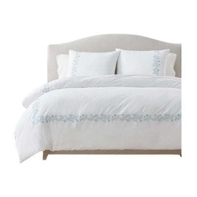 A neatly made bed with a light-colored headboard, featuring white bedding and pillowcases decorated with light blue floral embroidery, offers a Serena and Lily look for less.