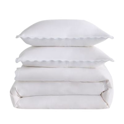 A neatly stacked set of white bedding, including two pillows with scalloped edges and folded sheets, offers a Serena and Lily look for less.