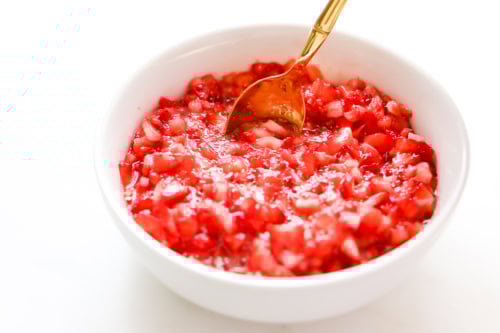 A white bowl filled with finely chopped strawberries and a gold-colored spoon resting inside.