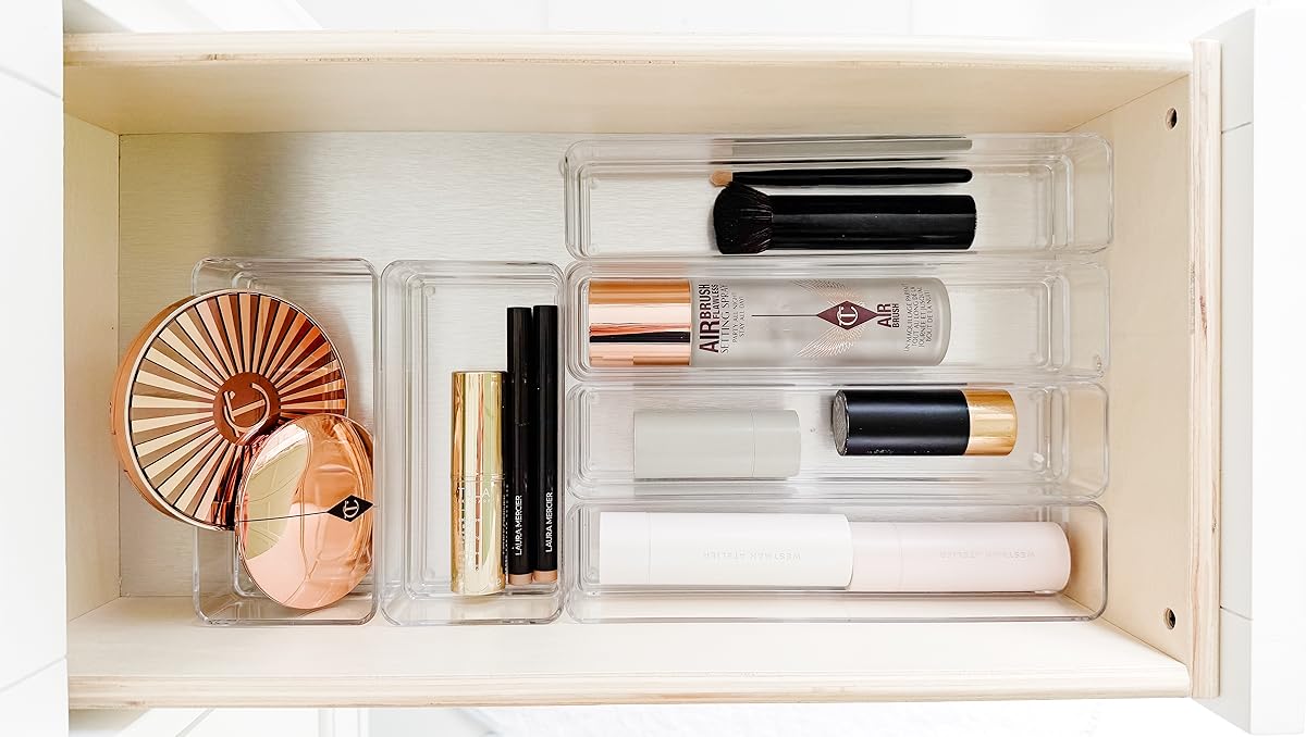 A neatly organized makeup drawer with brushes, compacts, lipsticks, and other cosmetic products arranged in clear acrylic trays.