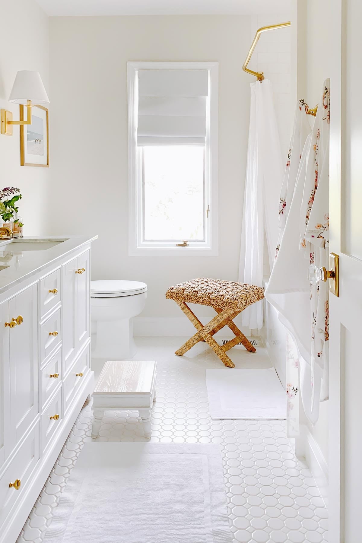 White bathroom featuring a vanity, toilet, a small woven stool, and a shower with a floral curtain.