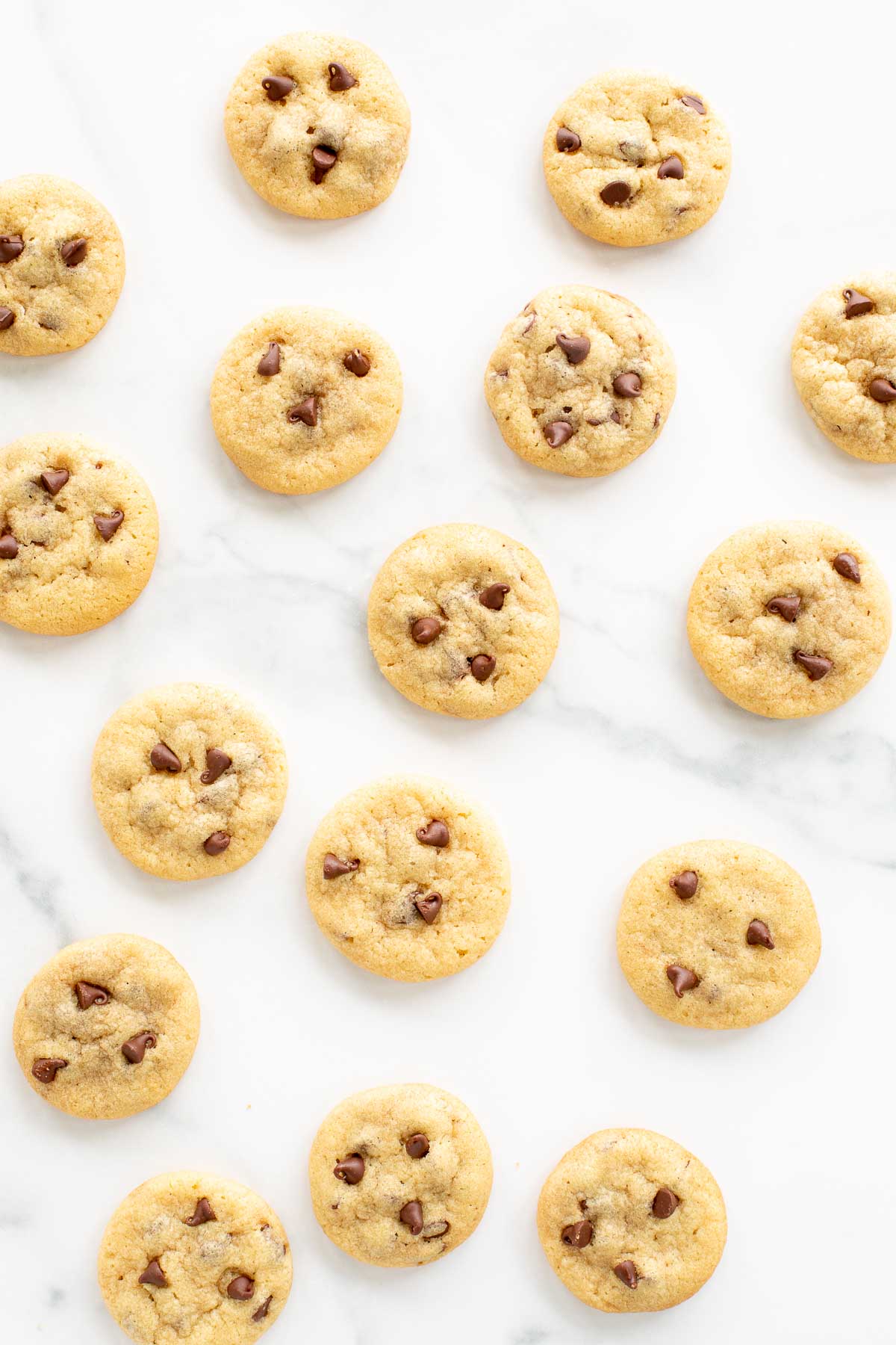 Chocolate chip cookies arranged in a scattered pattern on a white marble surface.