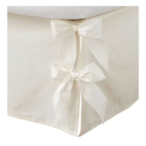 Close-up of a cream-colored fabric bed skirt with two large decorative bows tied on the corner.