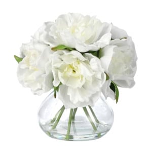 A clear glass vase holding a bouquet of large white peony flowers with green stems and leaves.
