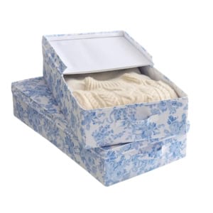 Two rectangular fabric storage boxes with blue floral patterns; one box contains a folded cream-colored sweater, and the other box is closed.