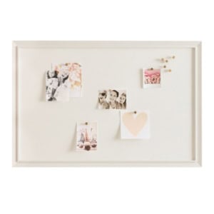 A white framed bulletin board with photos, a heart card, and push pins arranged across its surface.