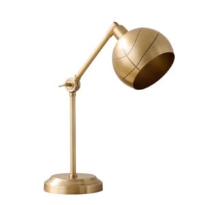 A brass adjustable desk lamp with a rounded shade and a pivoting arm, placed on a flat circular base, photographed against a white background.