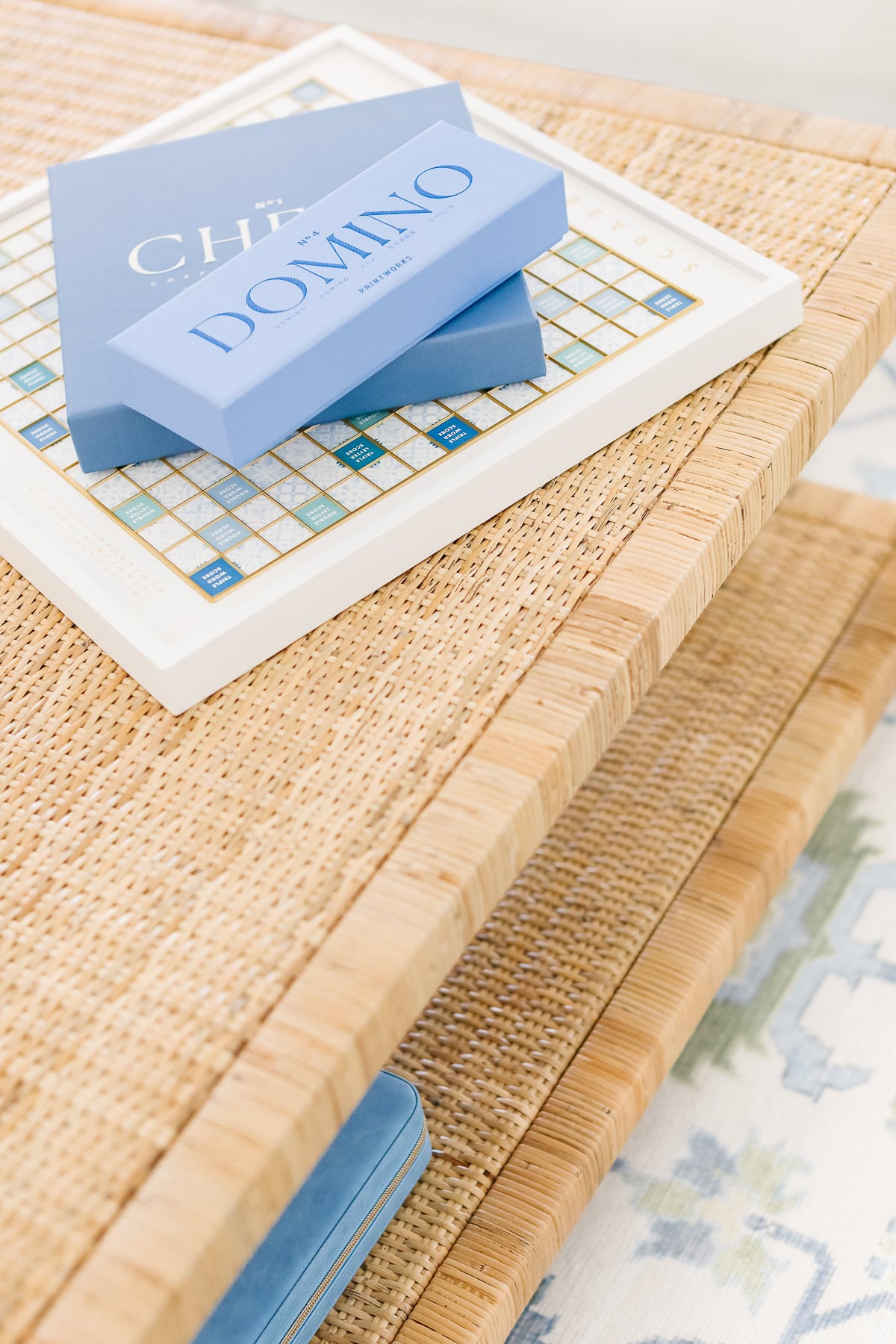 A white Scrabble board game on a woven table, with a blue Domino game box resting on top.
