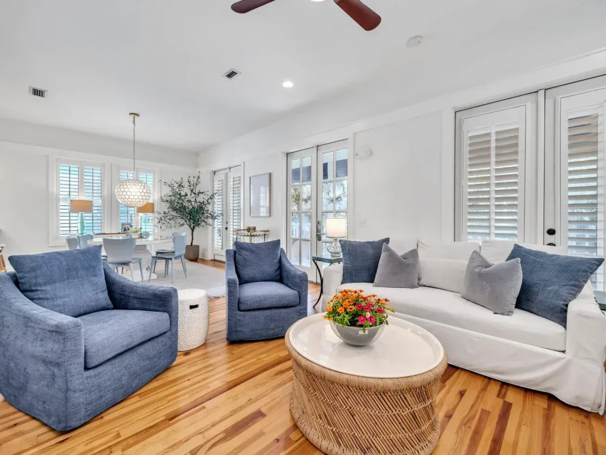 A living room with a white sofa and two blue armchairs arranged around a round wicker coffee table topped with a bowl of flowers.