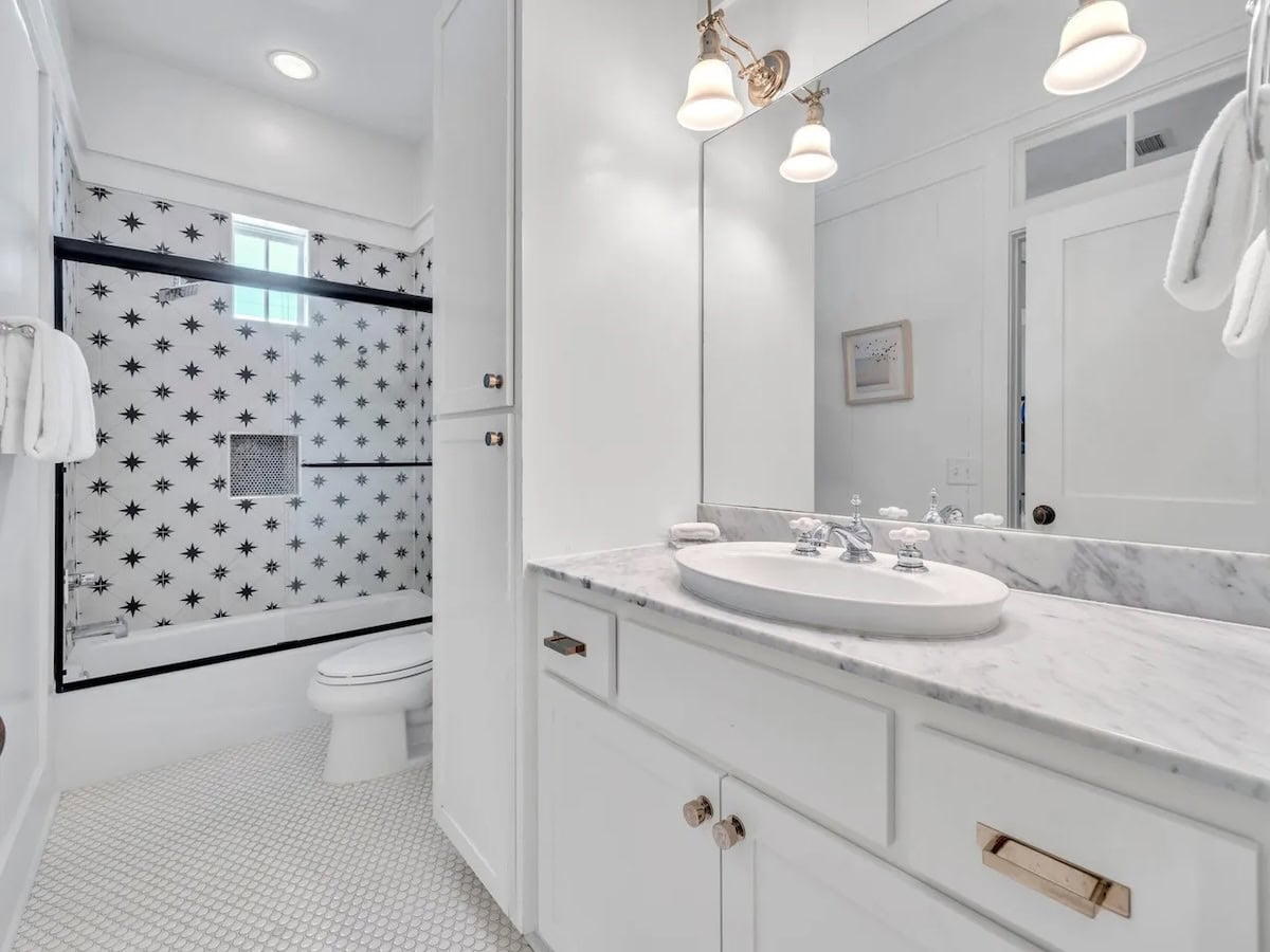 Bathroom with a marble-topped vanity and a tub-shower combination featuring white tiles with black star patterns.