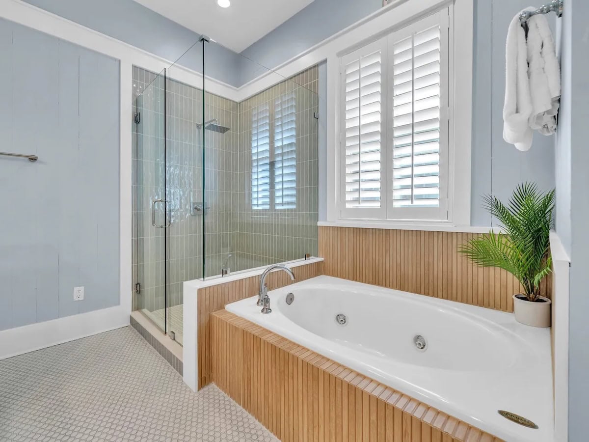 Bathroom with a jetted soaking tub in a wood-paneled surround, a glass-enclosed shower, and light blue walls.