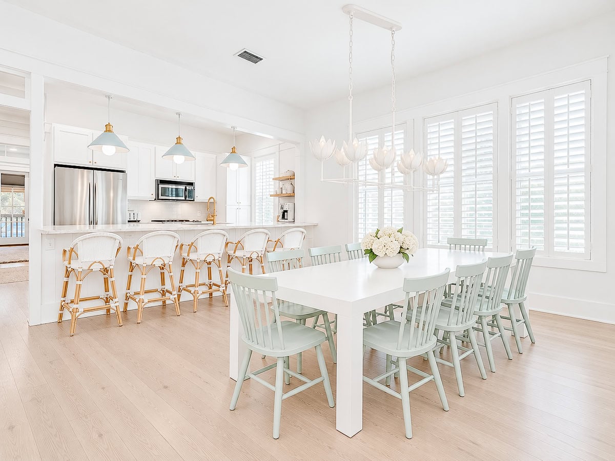 A bright, open-concept kitchen and dining area featuring a white dining table with light blue chairs and a kitchen island with four woven stools.