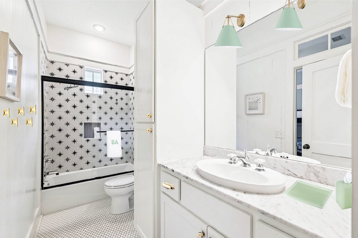 A bathroom with a marble-topped vanity and a tub-shower area featuring black and white star-patterned tile.
