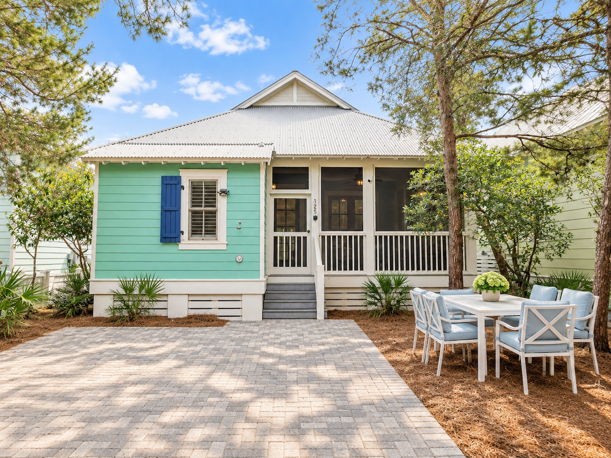 Turquoise cottage with white trim, a screened-in porch, and a stone patio with a dining set.