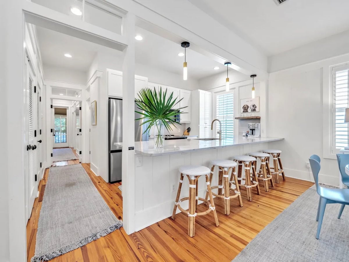 A kitchen island with five stools, opening into a hallway with wooden floors.