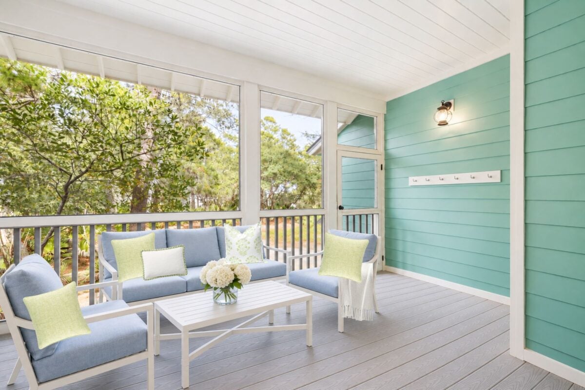 Screened porch with light blue sofa and armchairs, a white coffee table with flowers, and turquoise horizontal siding.