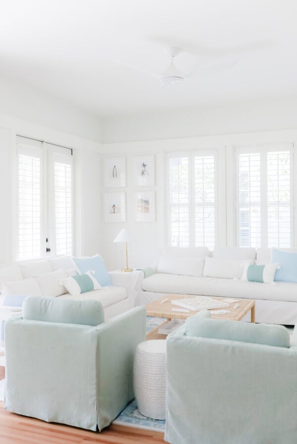 A bright living room with white sofas and two light blue armchairs arranged around a square wooden coffee table.