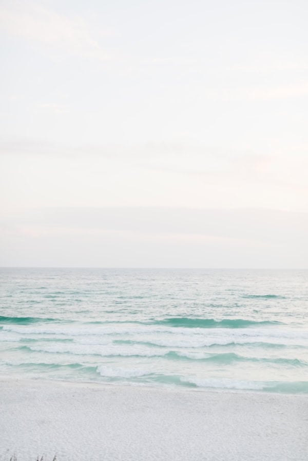 Gentle waves rolling onto a white sand beach under a pale, overcast sky.
