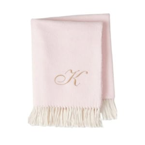 A folded light pink blanket with fringe trim and a gold embroidered letter K.