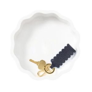 A key on a gold keyring with a navy blue scalloped leather fob inside a white, scalloped ceramic dish.