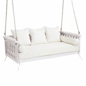 A white wooden porch swing hanging from chains with a cushioned seat, three square pillows, and two cylindrical bolster pillows.