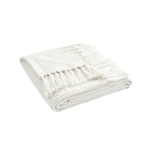 Folded white waffle-weave throw blanket with tasseled edges.
